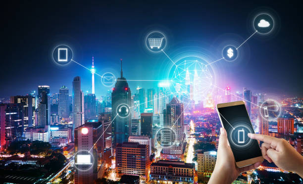 A hand holding a smartphone with icons representing smart city technology overlaying a cityscape background.